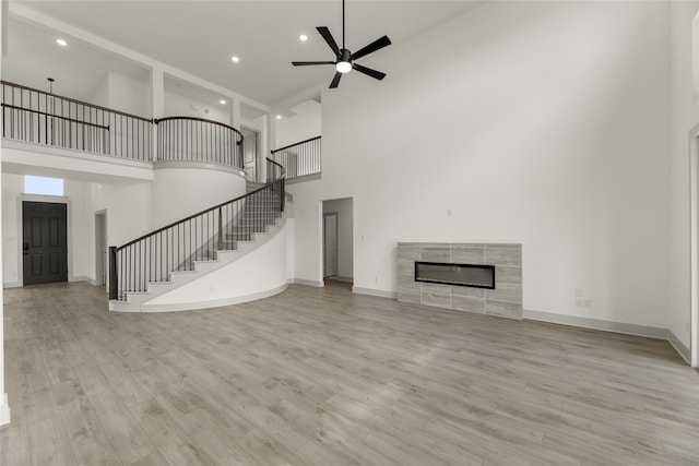 unfurnished living room featuring a towering ceiling, ceiling fan, light wood-type flooring, and a tile fireplace