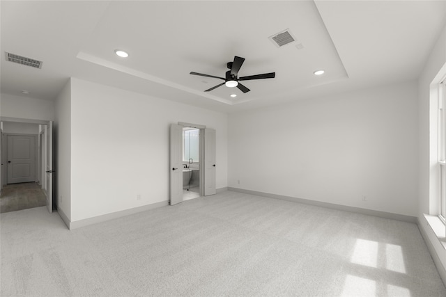 empty room with ceiling fan, a raised ceiling, and light colored carpet