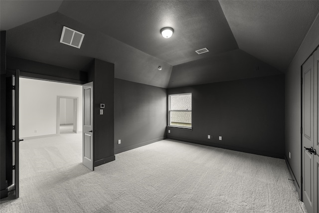 unfurnished bedroom featuring light colored carpet, a textured ceiling, a closet, and vaulted ceiling