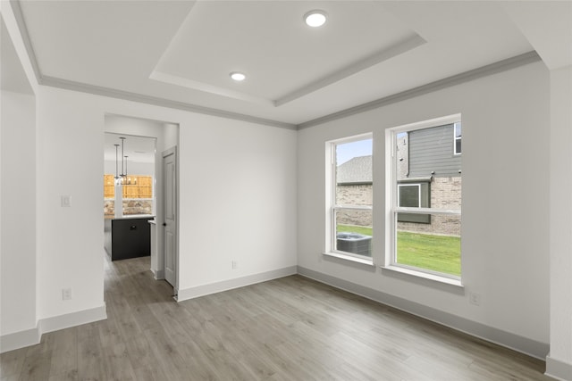 unfurnished room with ornamental molding, light wood-type flooring, and a tray ceiling