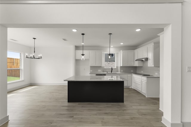 kitchen with a kitchen island, light hardwood / wood-style floors, white cabinetry, decorative light fixtures, and backsplash