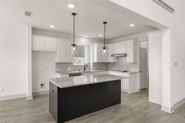 kitchen featuring white cabinets, hanging light fixtures, a kitchen island, light hardwood / wood-style flooring, and light stone countertops