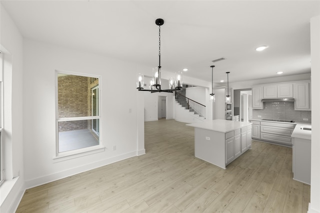 kitchen featuring backsplash, light hardwood / wood-style floors, a center island, hanging light fixtures, and white cabinets