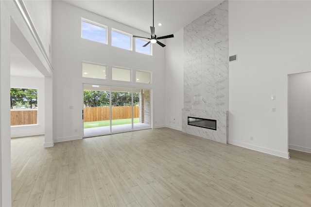 unfurnished living room with light hardwood / wood-style flooring, ceiling fan, a high ceiling, and a fireplace