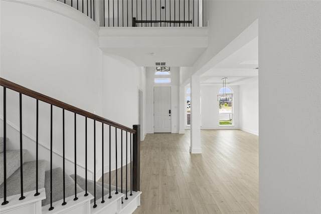 entryway featuring light wood-type flooring, a towering ceiling, and an inviting chandelier