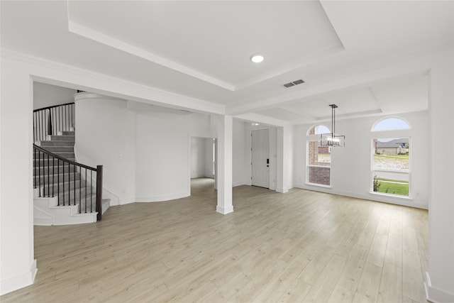 unfurnished living room featuring light wood-type flooring, a raised ceiling, and a chandelier