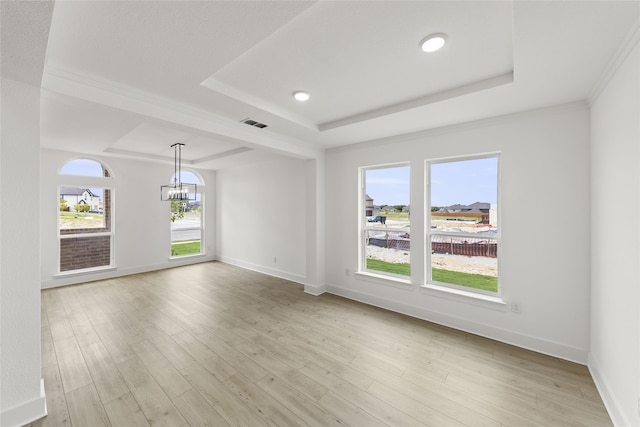 unfurnished room featuring a wealth of natural light, a raised ceiling, light wood-type flooring, and a chandelier