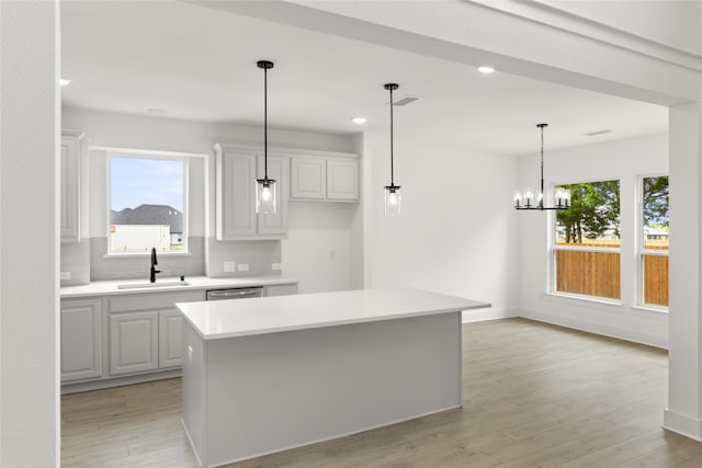 kitchen with light wood-type flooring, white cabinetry, a kitchen island, sink, and hanging light fixtures