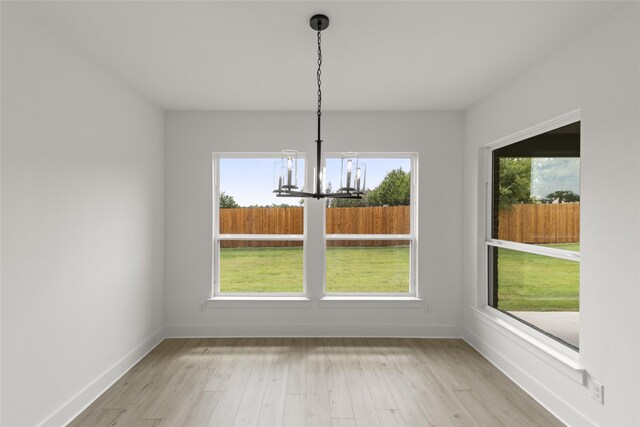 unfurnished dining area featuring a healthy amount of sunlight, an inviting chandelier, and light hardwood / wood-style floors