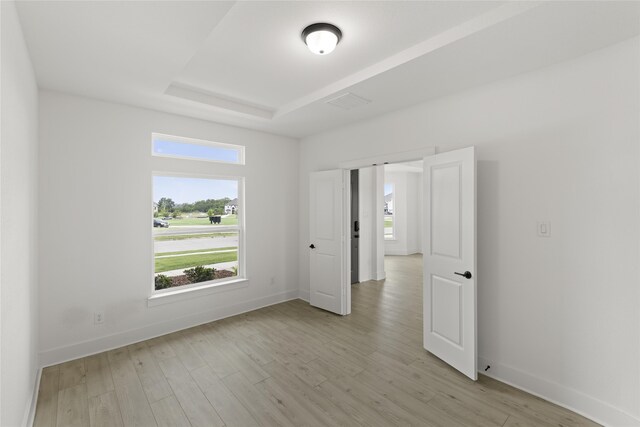 empty room featuring a tray ceiling and light hardwood / wood-style floors