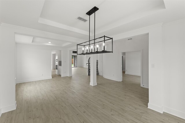 unfurnished dining area featuring ornamental molding, a raised ceiling, and light hardwood / wood-style floors