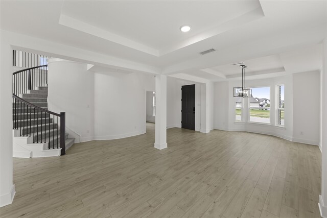 unfurnished living room with a chandelier, hardwood / wood-style flooring, and a raised ceiling