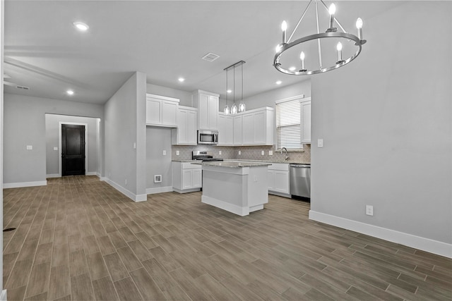 kitchen featuring appliances with stainless steel finishes, decorative light fixtures, light hardwood / wood-style flooring, a center island, and white cabinets