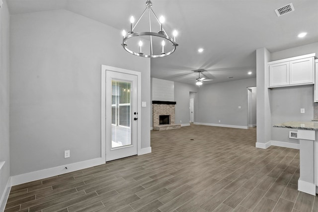 unfurnished living room with a brick fireplace, vaulted ceiling, dark hardwood / wood-style floors, and ceiling fan with notable chandelier