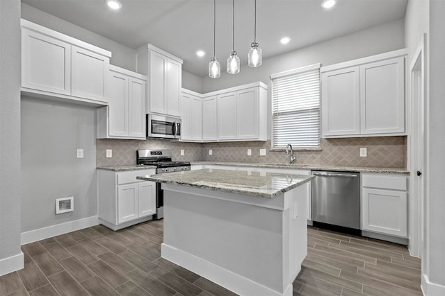 kitchen featuring light stone counters, stainless steel appliances, a kitchen island, pendant lighting, and white cabinets