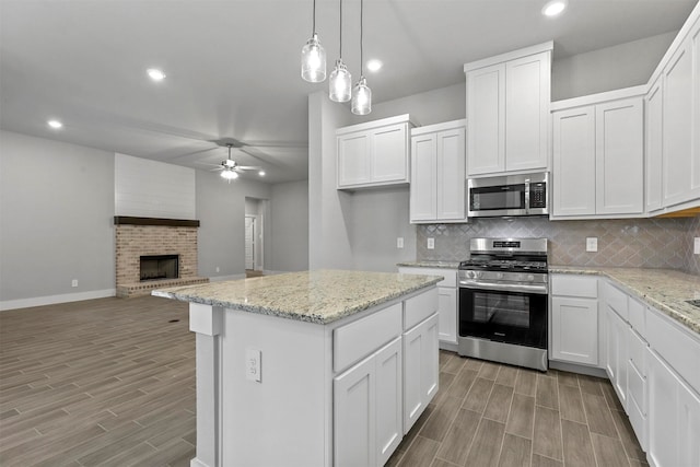 kitchen featuring white cabinetry, a brick fireplace, stainless steel appliances, and pendant lighting