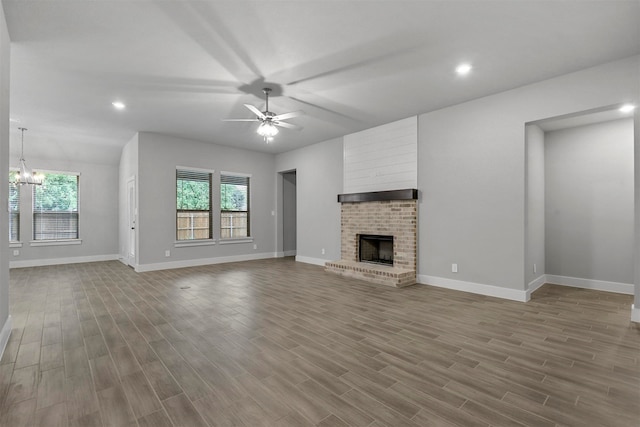 unfurnished living room with ceiling fan with notable chandelier, light hardwood / wood-style floors, and a fireplace