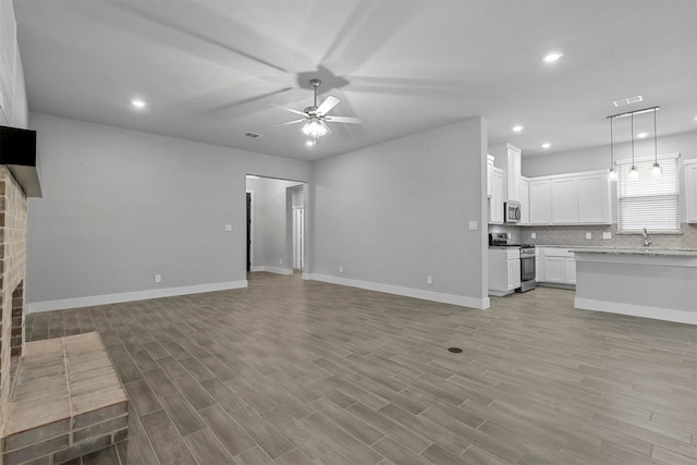 unfurnished living room with light wood-type flooring, sink, ceiling fan, and a fireplace