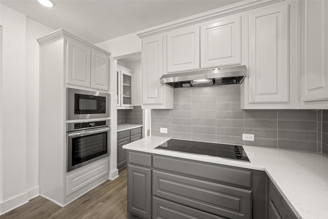 kitchen with white cabinetry, black appliances, dark hardwood / wood-style floors, light stone countertops, and backsplash