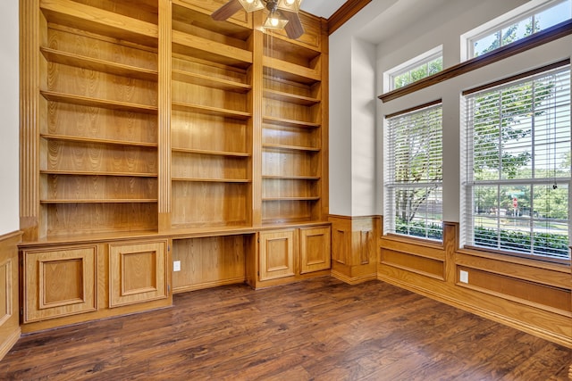 unfurnished office with ceiling fan, a healthy amount of sunlight, built in shelves, and dark wood-type flooring