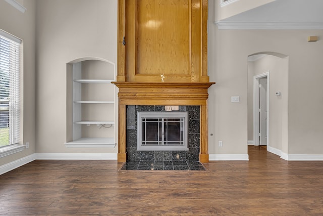 unfurnished living room with dark wood-type flooring, built in features, a high end fireplace, and crown molding