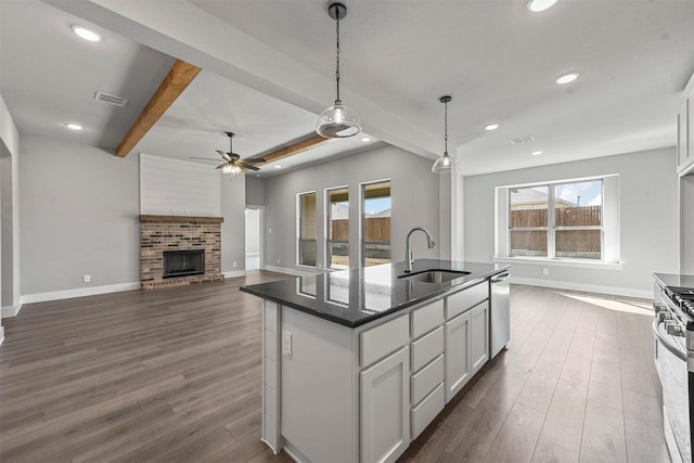 kitchen with a fireplace, a sink, appliances with stainless steel finishes, beamed ceiling, and dark wood finished floors