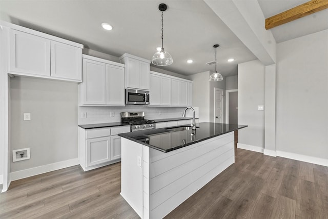 kitchen with stainless steel appliances, dark countertops, a sink, and wood finished floors