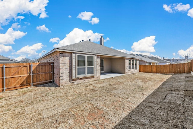 rear view of house featuring a patio, a fenced backyard, brick siding, a gate, and a chimney