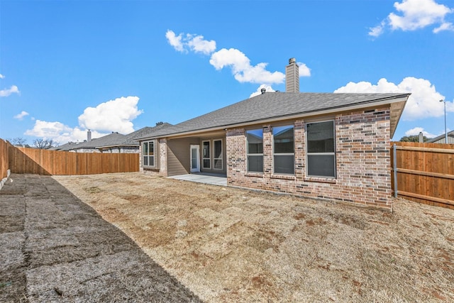 back of property featuring a patio, a fenced backyard, brick siding, roof with shingles, and a chimney