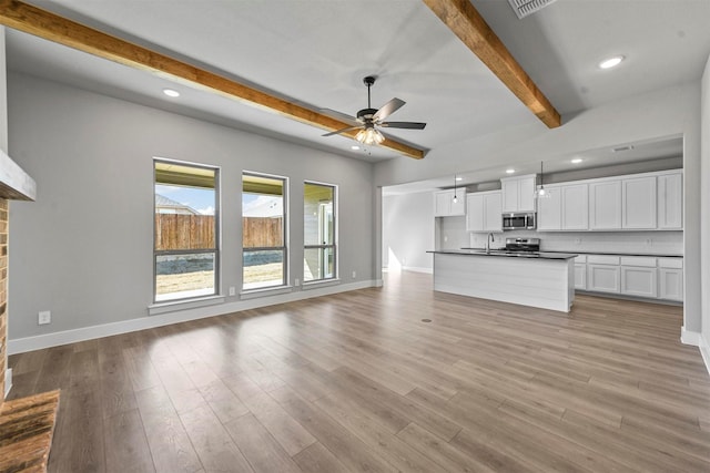 unfurnished living room featuring beam ceiling, light wood finished floors, recessed lighting, ceiling fan, and baseboards