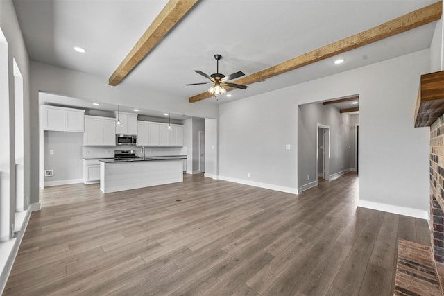 unfurnished living room with recessed lighting, wood finished floors, beam ceiling, and baseboards