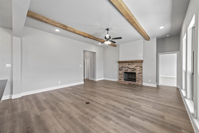 unfurnished living room featuring a fireplace, wood finished floors, a ceiling fan, baseboards, and beamed ceiling