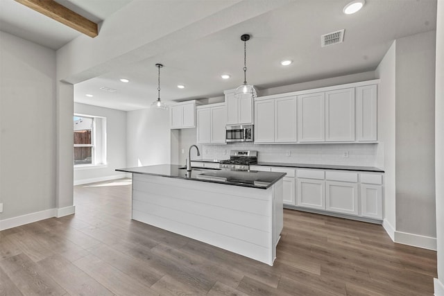 kitchen featuring stainless steel appliances, a sink, visible vents, tasteful backsplash, and dark countertops