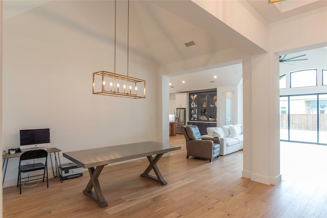 game room featuring a towering ceiling, light wood-type flooring, and ceiling fan with notable chandelier