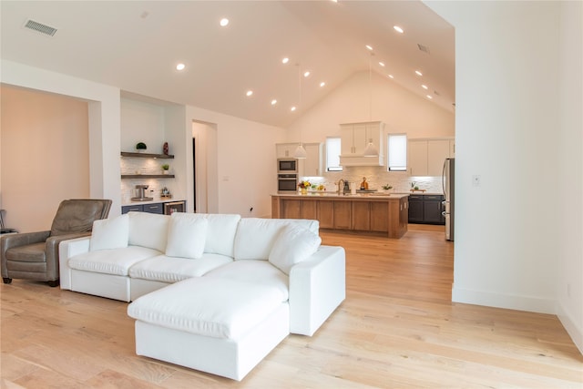 living room featuring high vaulted ceiling, sink, and light hardwood / wood-style flooring