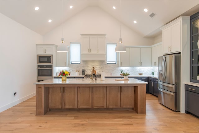 kitchen with light hardwood / wood-style floors, stainless steel appliances, white cabinets, a kitchen island with sink, and backsplash