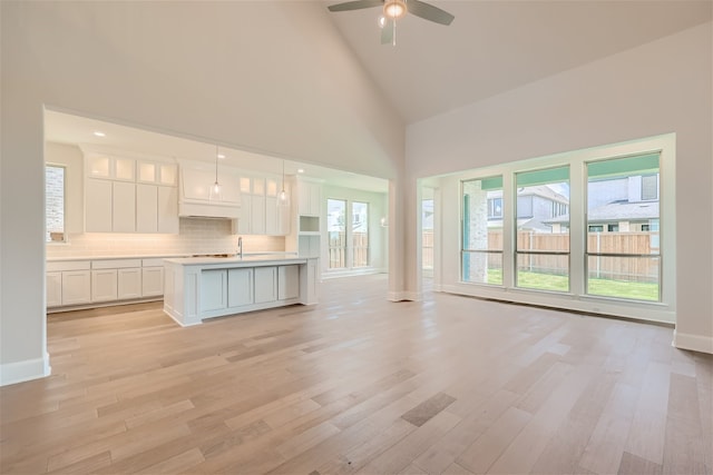 unfurnished living room with high vaulted ceiling, plenty of natural light, light hardwood / wood-style flooring, and sink