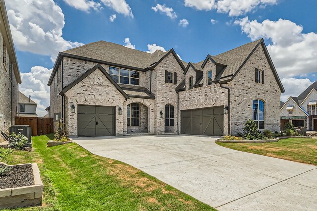 french provincial home featuring a front yard, a garage, and central air condition unit