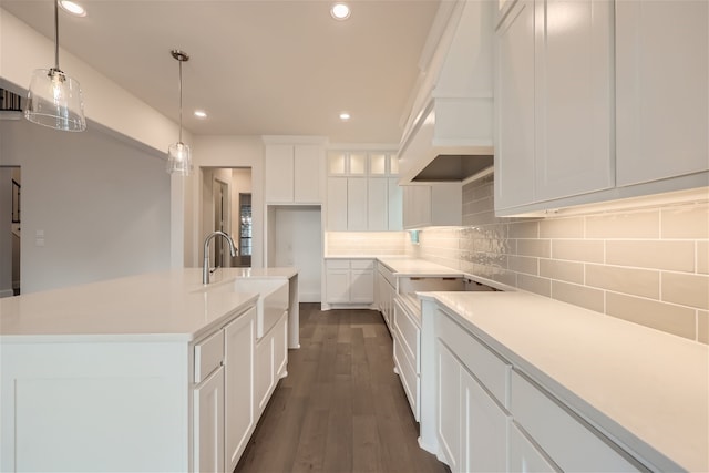 kitchen with backsplash, pendant lighting, a center island with sink, sink, and white cabinetry