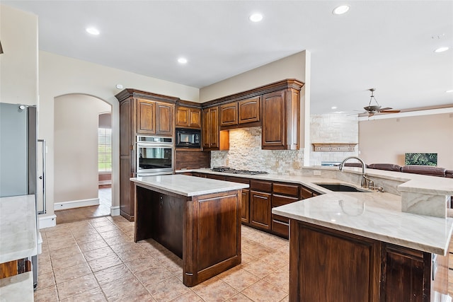 kitchen featuring sink, tasteful backsplash, a center island, appliances with stainless steel finishes, and light stone countertops