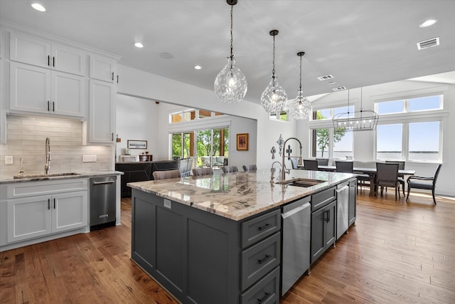 kitchen with dishwasher, dark wood-type flooring, hanging light fixtures, sink, and a kitchen island with sink