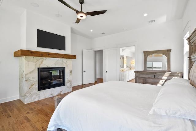 bedroom featuring a premium fireplace, ensuite bathroom, ceiling fan, and hardwood / wood-style floors