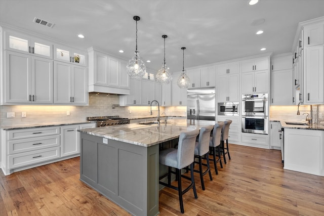 kitchen with built in appliances, light wood-type flooring, a large island, backsplash, and white cabinetry