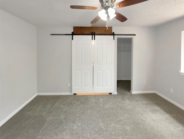 unfurnished bedroom featuring a barn door, ceiling fan, a closet, and carpet flooring