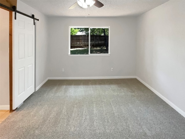 unfurnished bedroom featuring carpet flooring, a barn door, ceiling fan, and a textured ceiling