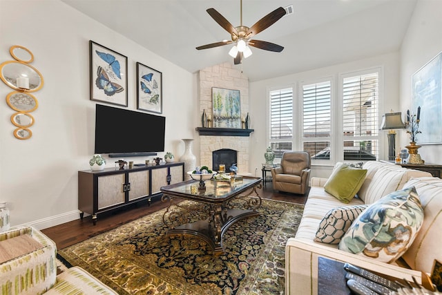 living room featuring ceiling fan, a stone fireplace, vaulted ceiling, and dark wood-type flooring