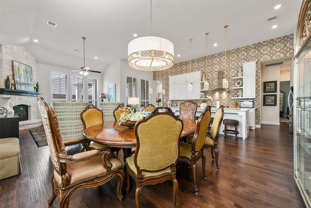 dining area with ceiling fan, a stone fireplace, dark hardwood / wood-style flooring, and vaulted ceiling