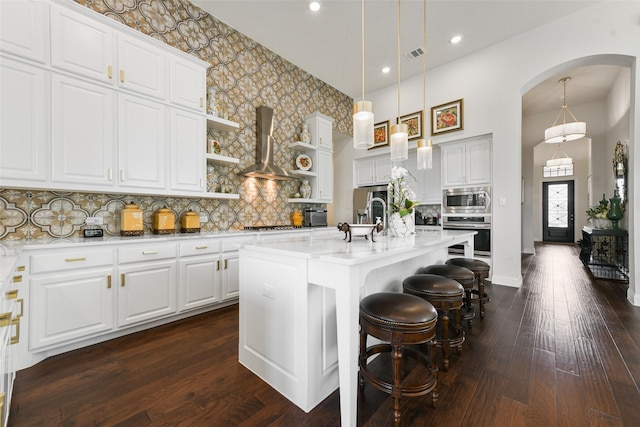 kitchen featuring dark hardwood / wood-style flooring, white cabinets, an island with sink, wall chimney exhaust hood, and backsplash