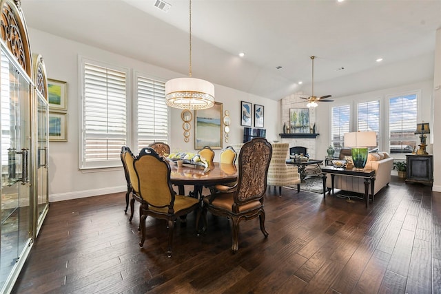 dining area featuring dark hardwood / wood-style flooring, a wealth of natural light, lofted ceiling, and a stone fireplace