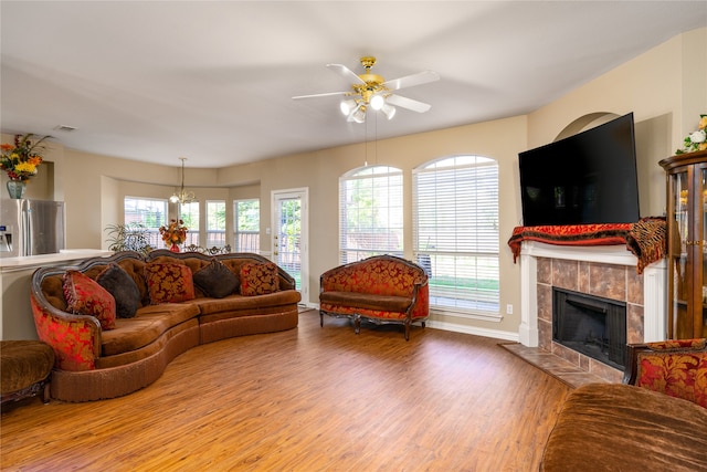 living room featuring wood-type flooring, a tile fireplace, and ceiling fan with notable chandelier